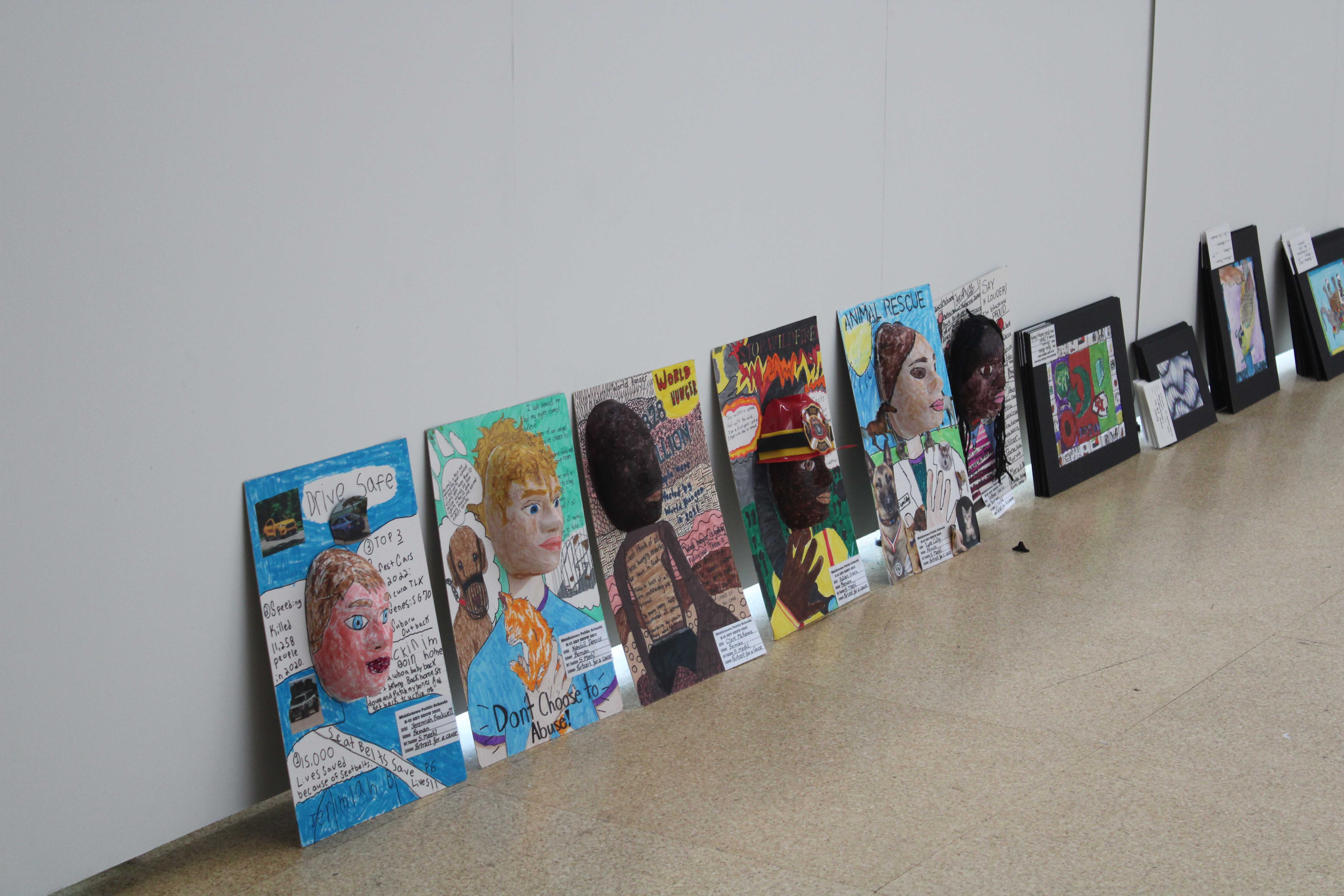 Pieces of artwork are lined up on the floor, set up against the wall, ready to be hung for the upcoming art show